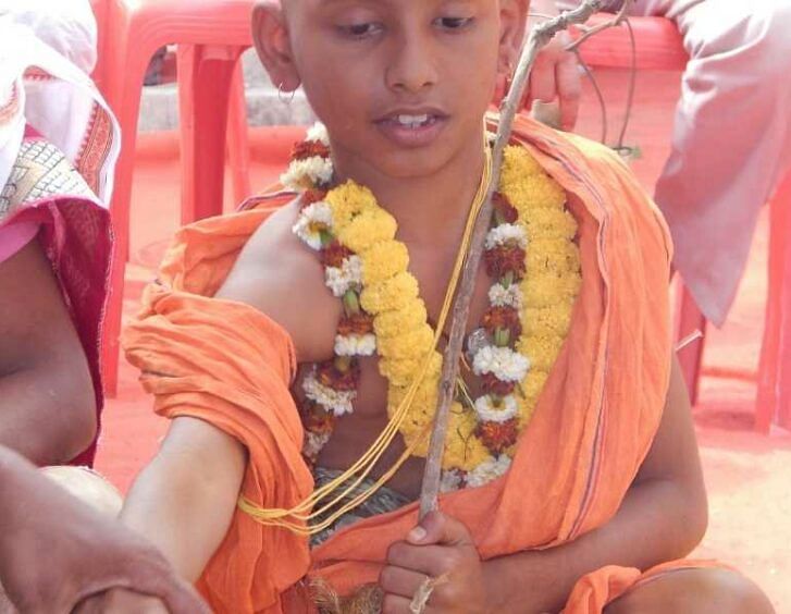 A Nepali boy in an orange robe is holding a flower.